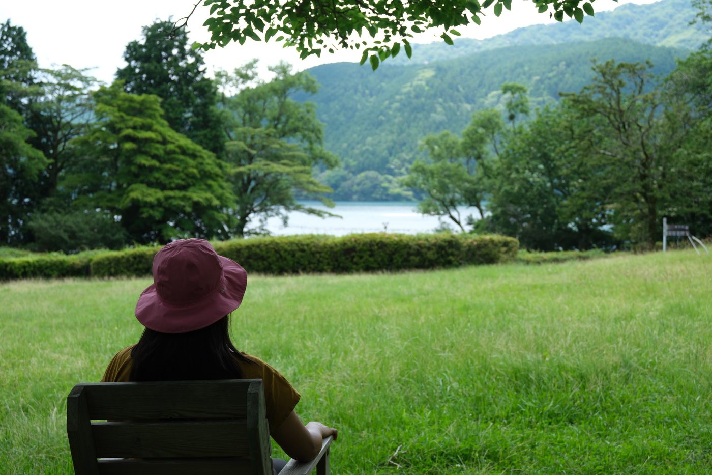 A guest sitting quietly on a bench facing Lake Ashi and the mountains